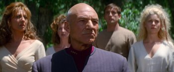 Movie still from “Star Trek: Insurrection” (1998), directed by Jonathan Frakes – A man in a purple jacket with two women in the background; Close Up shot, Over the shoulder angle