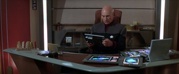 Movie still from “Star Trek: Insurrection” (1998), directed by Jonathan Frakes – A man sitting at a desk with a tablet; Medium shot, High angle