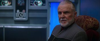 Movie still from “Star Trek: Insurrection” (1998), directed by Jonathan Frakes – An older man with a gray beard is looking at the camera; Close Up shot, Over the shoulder angle