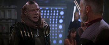 Movie still from “Star Trek: Insurrection” (1998), directed by Jonathan Frakes – A man in a star trek costume in front of a group of people; Close Up shot, Over the shoulder angle