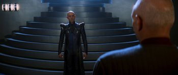Movie still from “Star Trek: Nemesis” (2002), directed by Stuart Baird – A man in a black suit standing in front of some stairs; Medium shot, Over the shoulder angle