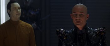 Movie still from “Star Trek: Nemesis” (2002), directed by Stuart Baird – A bald man in a leather jacket holding a robotic arm; Close Up shot, Over the shoulder angle