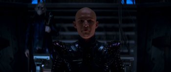 Movie still from “Star Trek: Nemesis” (2002), directed by Stuart Baird – A bald man in a black suit is posing for a picture; Medium shot, Low angle
