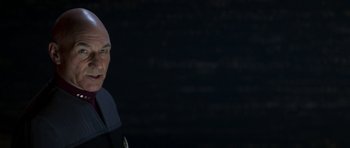 Movie still from “Star Trek: Nemesis” (2002), directed by Stuart Baird – A man with a bald head is standing in front of a dark background; Close Up shot, Over the shoulder angle