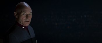 Movie still from “Star Trek: Nemesis” (2002), directed by Stuart Baird – A man with a bald head is standing in the dark; Close Up shot, Over the shoulder angle