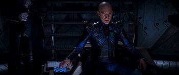 Movie still from “Star Trek: Nemesis” (2002), directed by Stuart Baird – A bald man in a blue suit sitting on a chair; Medium shot, High angle
