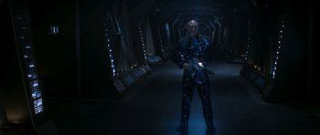 Movie still from “Star Trek: Nemesis” (2002), directed by Stuart Baird – A man standing in a dark room holding a gun; Wide shot, Overhead angle