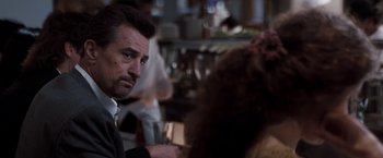 Movie still from “Heat” (1995), directed by Michael Mann – A person sitting at a table holding a drink; Close Up shot, Over the shoulder angle