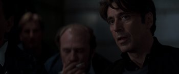 Movie still from “Heat” (1995), directed by Michael Mann – A man smoking a cigarette next to another man in a dark room; Close Up shot, Over the shoulder angle