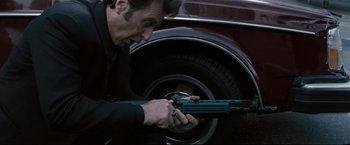 Movie still from “Heat” (1995), directed by Michael Mann – A man holding a gun in front of an old car tire; Close Up shot, Low angle
