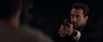 Movie still from “Heat” (1995), directed by Michael Mann – A man in a suit and tie holding a gun in his hand; Close Up shot, Over the shoulder angle