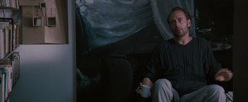 Movie still from “Heat” (1995), directed by Michael Mann – A man sitting on a chair holding a cup; Medium shot, Low angle