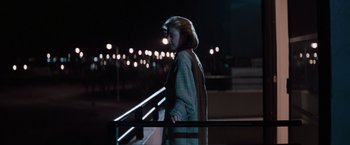 Movie still from “Heat” (1995), directed by Michael Mann – A woman standing on a railing at night with lights in the background; Wide shot, Low angle