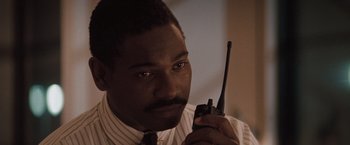Movie still from “Heat” (1995), directed by Michael Mann – A man holding a walkie talkie while wearing a tie; Close Up shot, Low angle