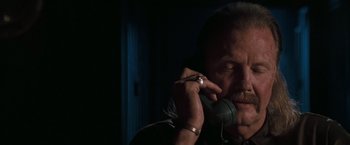Movie still from “Heat” (1995), directed by Michael Mann – An older man talking on a phone while wearing a pair of headphones; Close Up shot, Low angle