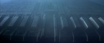 Movie still from “Stargate” (1994), directed by Roland Emmerich – A large building in the middle of a foggy day; Extreme Wide shot, Overhead angle