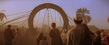 Movie still from “Stargate” (1994), directed by Roland Emmerich – A group of people standing around a large structure; Wide shot, Over the shoulder angle