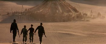 Movie still from “Stargate” (1994), directed by Roland Emmerich – Two men walking in the desert near a crowd of people; Extreme Wide shot, Over the shoulder angle