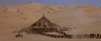 Movie still from “Stargate” (1994), directed by Roland Emmerich – A group of people standing around a tent in the desert; Extreme Wide shot, High angle