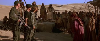 Movie still from “Stargate” (1994), directed by Roland Emmerich – A group of people standing in the desert; Wide shot, Over the shoulder angle