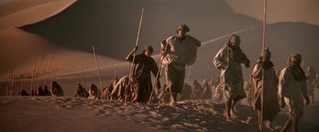Movie still from “Stargate” (1994), directed by Roland Emmerich – A group of people walking through the sand dunes; Wide shot, Low angle