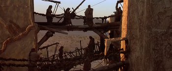 Movie still from “Stargate” (1994), directed by Roland Emmerich – A group of people standing on top of a wooden structure; Wide shot, Low angle
