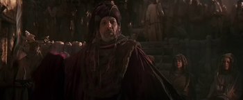 Movie still from “Stargate” (1994), directed by Roland Emmerich – A man wearing a red and purple robe and a hat; Medium shot, High angle