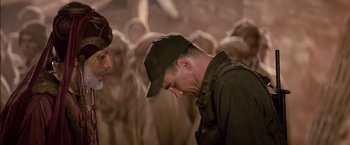 Movie still from “Stargate” (1994), directed by Roland Emmerich – A man in a hat is standing in front of a group of people; Close Up shot, Over the shoulder angle