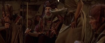 Movie still from “Stargate” (1994), directed by Roland Emmerich – An old man in a turban is holding a plate of food; Medium shot, High angle