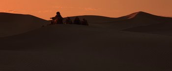 Movie still from “Stargate” (1994), directed by Roland Emmerich – A group of people sitting on top of a sand dune; Extreme Wide shot, Low angle