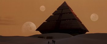 Movie still from “Stargate” (1994), directed by Roland Emmerich – Three people are standing in front of a large pyramid; Extreme Wide shot, Low angle