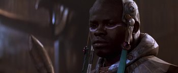 Movie still from “Stargate” (1994), directed by Roland Emmerich – A man in a black outfit with long earrings; Close Up shot, Low angle