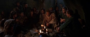 Movie still from “Stargate” (1994), directed by Roland Emmerich – A group of people sitting around a fire; Wide shot, High angle