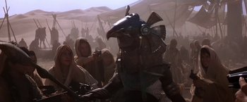 Movie still from “Stargate” (1994), directed by Roland Emmerich – A group of people standing in a field; Medium shot, Over the shoulder angle