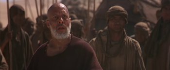 Movie still from “Stargate” (1994), directed by Roland Emmerich – An old man with a beard and a beard is standing in front of another man; Close Up shot, Low angle