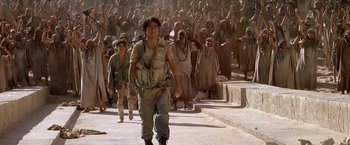 Movie still from “Stargate” (1994), directed by Roland Emmerich – A group of people walking down a sidewalk; Wide shot, Low angle