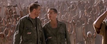Movie still from “Stargate” (1994), directed by Roland Emmerich – Two men standing next to each other in front of a crowd of people; Medium shot, Low angle