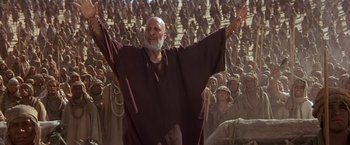 Movie still from “Stargate” (1994), directed by Roland Emmerich – An old man with a long beard is standing in front of a group of people; Medium shot, Low angle