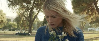 A beautiful blonde woman holding a flower in a park