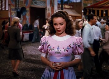 Movie still from “State Fair” (1945), directed by Walter Lang – A woman wearing a pink dress with flowers on it in front of a crowd of onlookers; Medium shot, Low angle