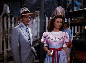 Movie still from “State Fair” (1945), directed by Walter Lang – A man and a woman standing next to each other in front of a picket fence; Medium shot, Over the shoulder angle