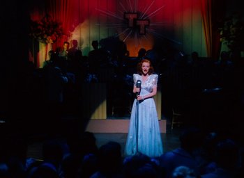 Movie still from “State Fair” (1945), directed by Walter Lang – A woman in a white dress is singing into a microphone; Wide shot, Low angle