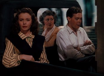 Movie still from “State Fair” (1945), directed by Walter Lang – A woman sitting in the back of a car next to a man and a woman; Medium shot, High angle