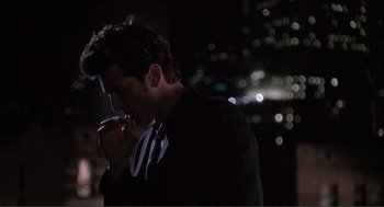 Movie still from “State of Grace” (1990), directed by Phil Joanou – A man in a black suit is smoking a cigarette; Medium shot, Over the shoulder angle