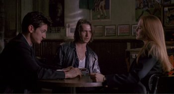 Movie still from “State of Grace” (1990), directed by Phil Joanou – A man sitting at a table with two other men; Medium shot, Over the shoulder angle