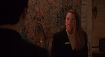 Movie still from “State of Grace” (1990), directed by Phil Joanou – A woman standing in front of a wall with a painting on it; Medium shot, Over the shoulder angle