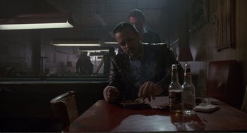 Movie still from “State of Grace” (1990), directed by Phil Joanou – A man sitting at a table smoking a cigarette; Medium shot, Low angle