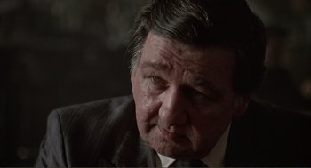 Movie still from “State of Grace” (1990), directed by Phil Joanou – An older man wearing a suit and a tie; Close Up shot, Over the shoulder angle