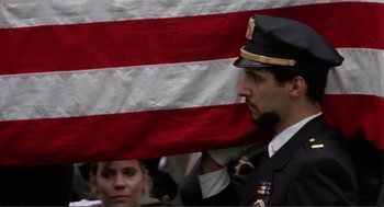 Movie still from “State of Grace” (1990), directed by Phil Joanou – A man in uniform holding an american flag in front of a crowd; Close Up shot, Low angle