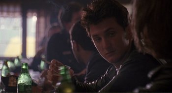 Movie still from “State of Grace” (1990), directed by Phil Joanou – A man sitting at a table with a cigarette in his hand; Close Up shot, Over the shoulder angle